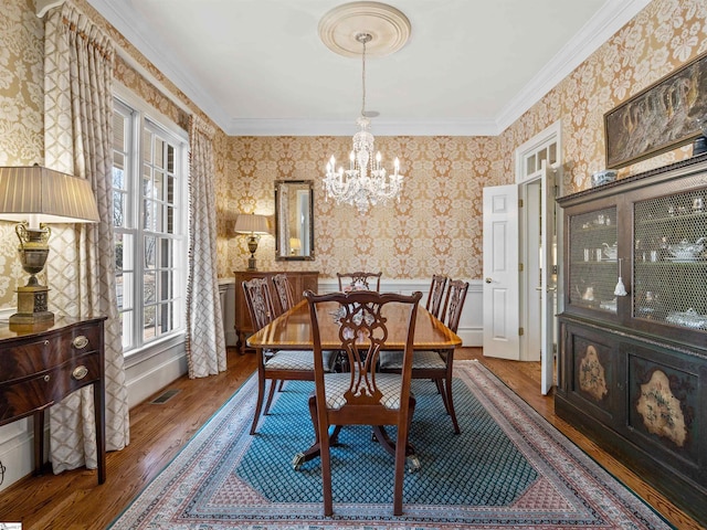 dining area with wood finished floors, visible vents, wallpapered walls, an inviting chandelier, and crown molding