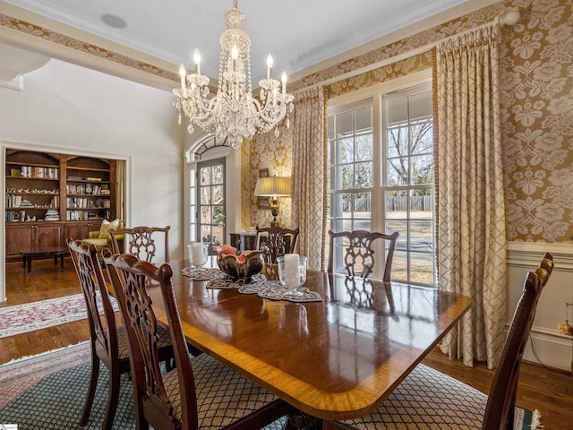 dining space with wallpapered walls, ornamental molding, a chandelier, and wood finished floors