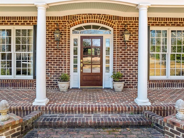 view of exterior entry with a porch and brick siding