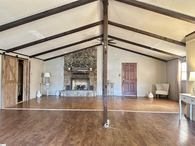 unfurnished living room featuring vaulted ceiling with beams, a barn door, a fireplace, wood finished floors, and a ceiling fan