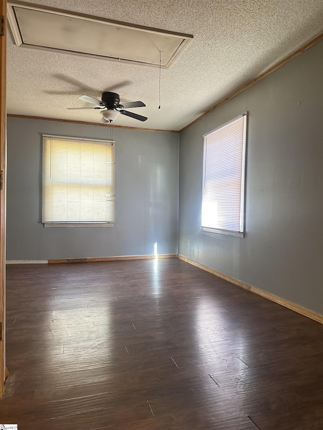 empty room featuring a textured ceiling, wood finished floors, attic access, and baseboards