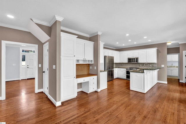 kitchen featuring dark countertops, backsplash, appliances with stainless steel finishes, white cabinetry, and a peninsula