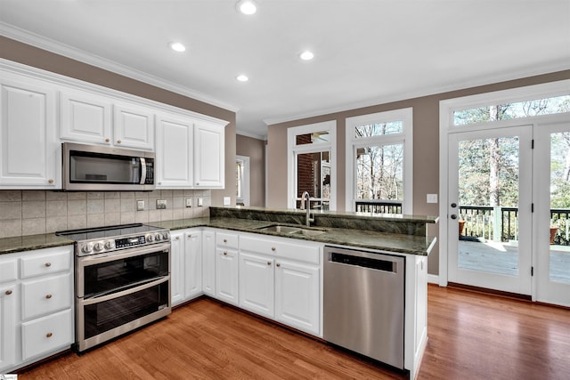 kitchen featuring decorative backsplash, appliances with stainless steel finishes, a peninsula, crown molding, and a sink