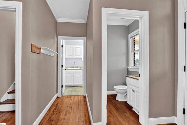 corridor featuring light wood-style floors, crown molding, and baseboards