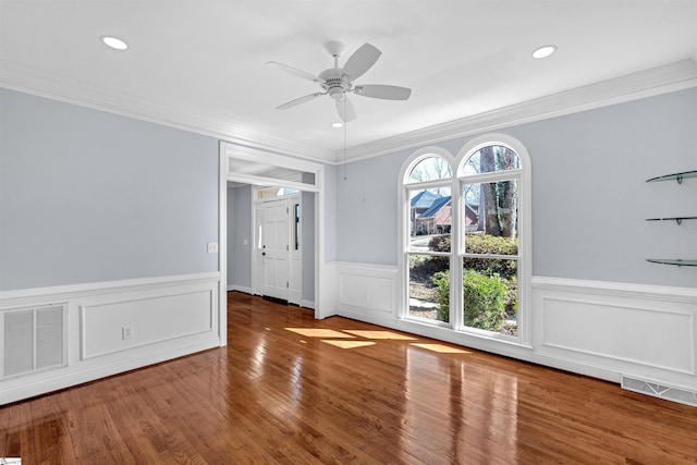 interior space featuring crown molding, visible vents, wainscoting, ceiling fan, and wood finished floors