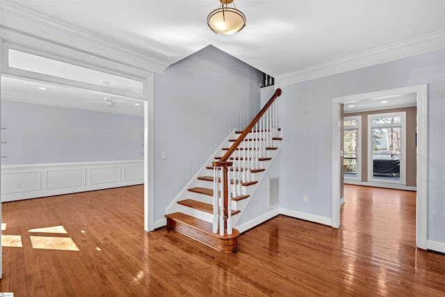 stairway with ornamental molding, hardwood / wood-style flooring, visible vents, and baseboards