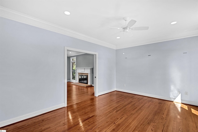 spare room featuring baseboards, a ceiling fan, a glass covered fireplace, ornamental molding, and wood finished floors