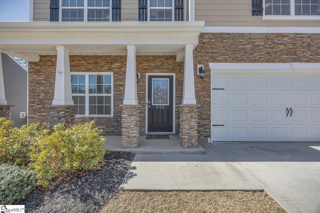 view of exterior entry with covered porch, concrete driveway, stone siding, and an attached garage