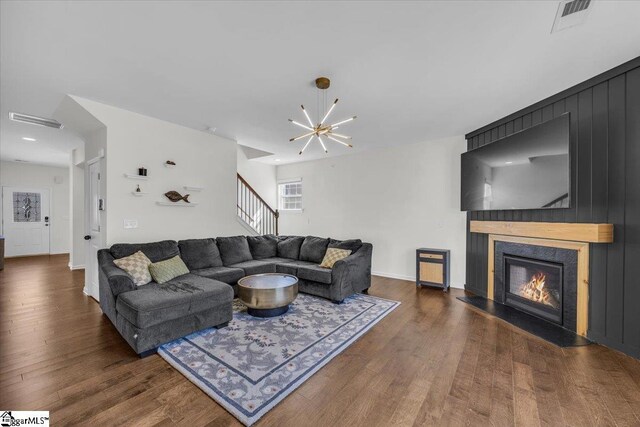 living area featuring visible vents, wood finished floors, stairs, a fireplace, and a notable chandelier