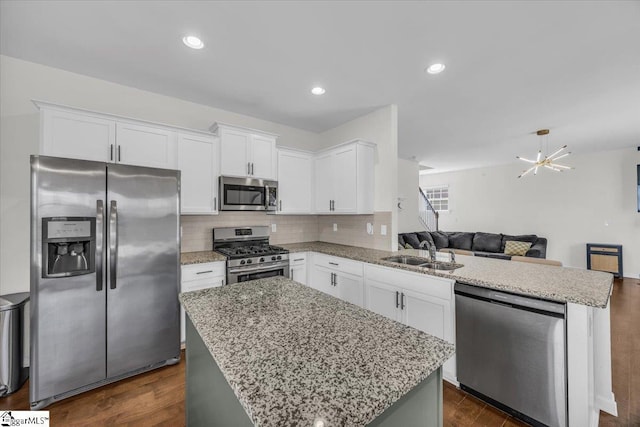 kitchen with stainless steel appliances, a peninsula, a sink, open floor plan, and light stone countertops