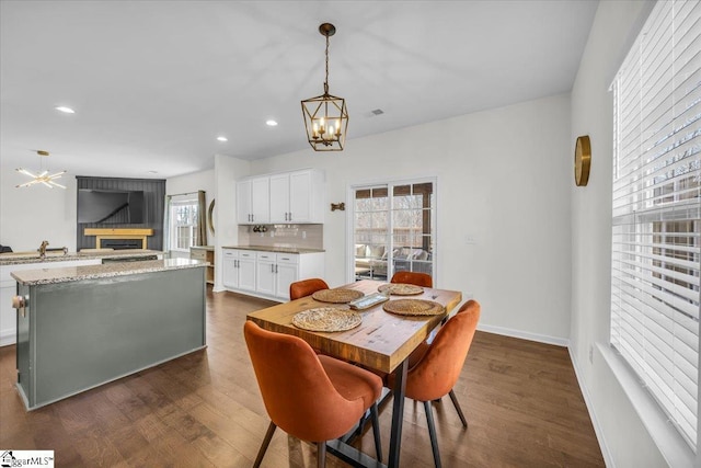 dining room with an inviting chandelier, a fireplace, dark wood-type flooring, and recessed lighting