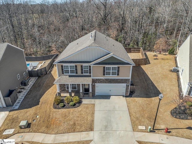 view of front facade with driveway, a garage, board and batten siding, fence, and a wooded view