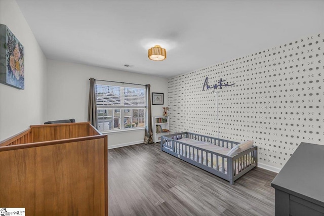 bedroom with a nursery area, visible vents, dark wood finished floors, and baseboards