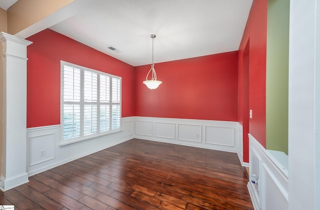 unfurnished dining area featuring visible vents, dark wood-type flooring, wainscoting, and decorative columns