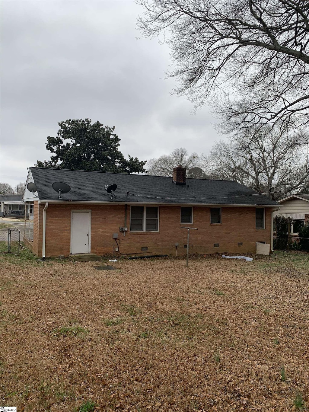 back of property featuring crawl space, brick siding, fence, and a chimney