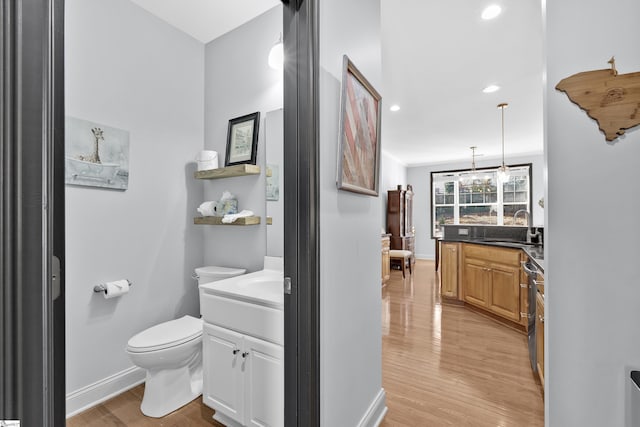 bathroom with baseboards, toilet, wood finished floors, vanity, and recessed lighting