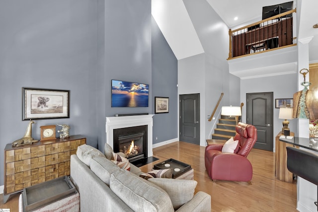 living area with stairway, a towering ceiling, light wood-style floors, a fireplace with flush hearth, and baseboards