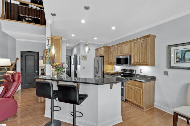 kitchen with a peninsula, a breakfast bar, appliances with stainless steel finishes, dark stone counters, and light wood finished floors