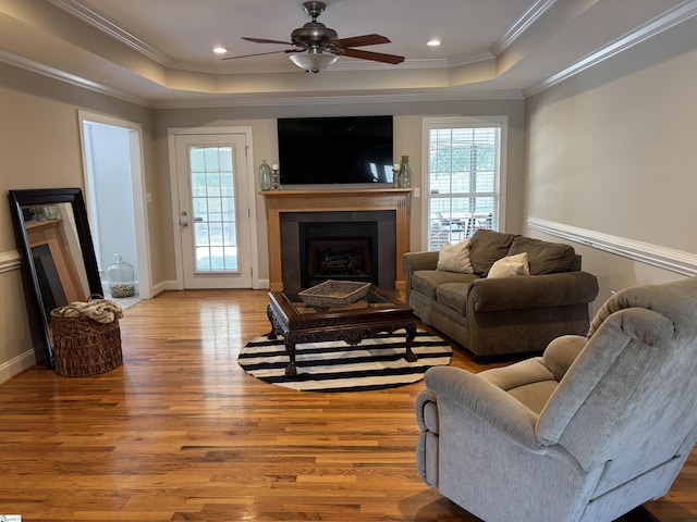 living room featuring ornamental molding, a tray ceiling, a fireplace, and wood finished floors