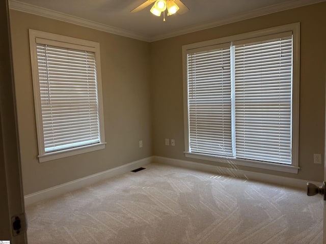 carpeted empty room featuring ceiling fan, ornamental molding, visible vents, and baseboards