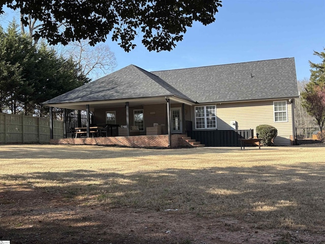 back of house with a porch, roof with shingles, and fence