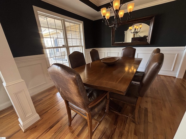 dining area with a decorative wall, a wainscoted wall, wood finished floors, ornamental molding, and an inviting chandelier