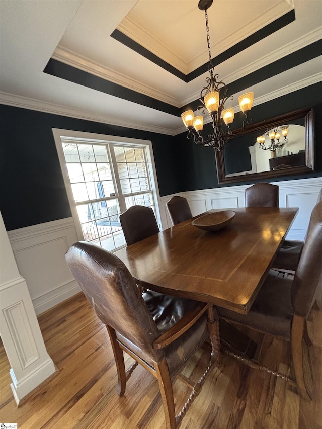 dining room with ornamental molding, a raised ceiling, a wainscoted wall, and wood finished floors