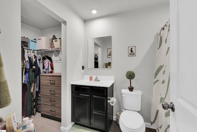 bathroom featuring a spacious closet, vanity, toilet, and baseboards