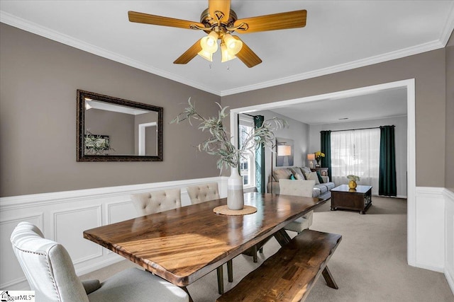 dining room featuring ornamental molding, wainscoting, light colored carpet, and a ceiling fan