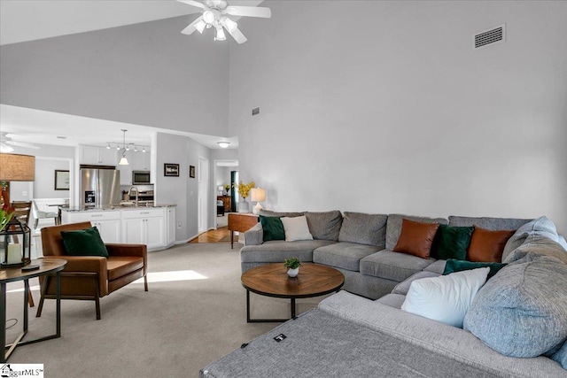 living area featuring light carpet, a towering ceiling, visible vents, and ceiling fan with notable chandelier