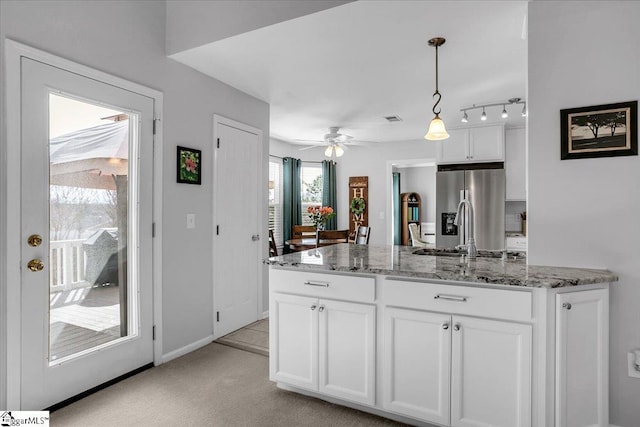 kitchen with white cabinets, stainless steel fridge with ice dispenser, light stone countertops, pendant lighting, and a sink