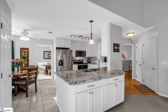 kitchen with appliances with stainless steel finishes, white cabinetry, a sink, and light stone counters