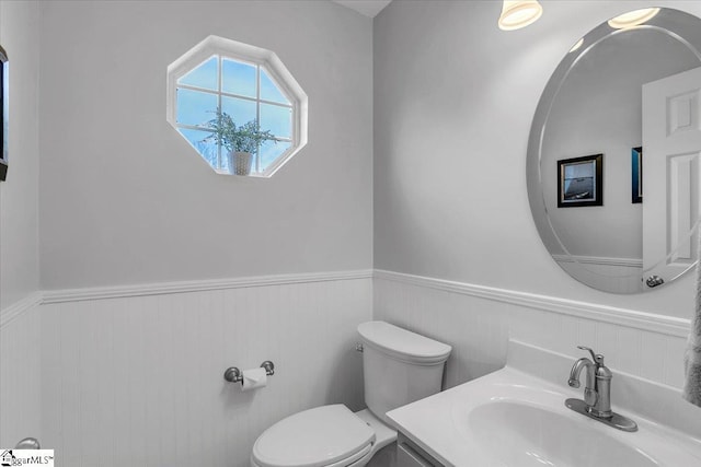 half bathroom with wainscoting, vanity, and toilet