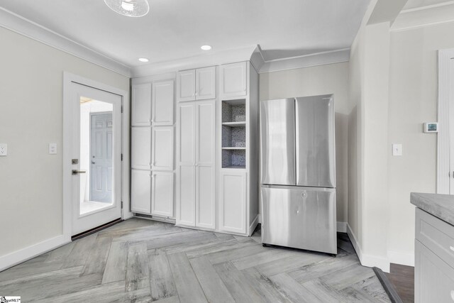 kitchen featuring baseboards, ornamental molding, freestanding refrigerator, and white cabinetry