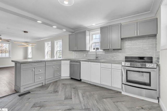 kitchen with a peninsula, stainless steel appliances, a sink, and gray cabinetry