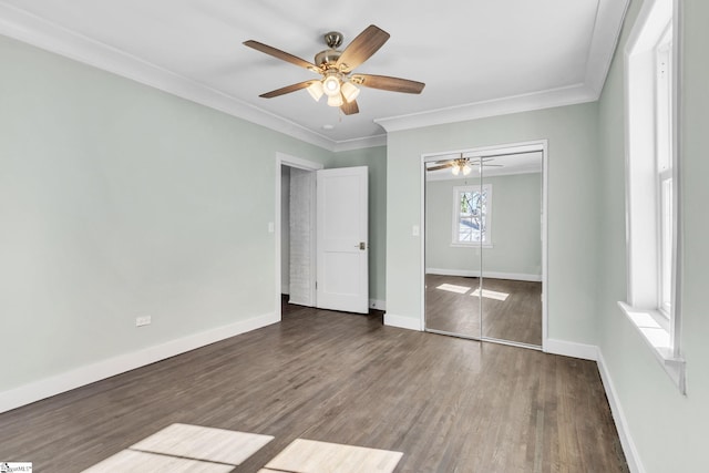 unfurnished bedroom with baseboards, ceiling fan, wood finished floors, crown molding, and a closet