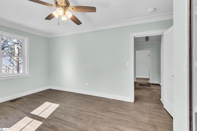 spare room featuring ornamental molding, visible vents, baseboards, and wood finished floors