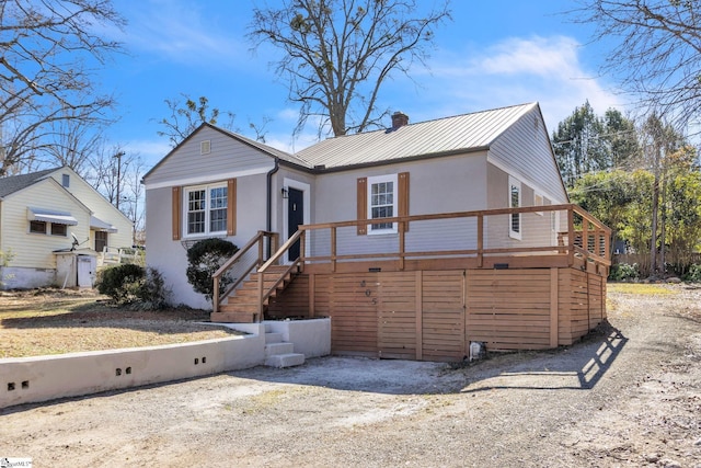 view of front of house with a deck, metal roof, a chimney, and stucco siding