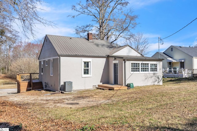 back of house featuring a lawn, a chimney, metal roof, cooling unit, and stucco siding