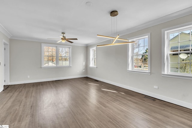 empty room featuring a healthy amount of sunlight, visible vents, crown molding, and wood finished floors