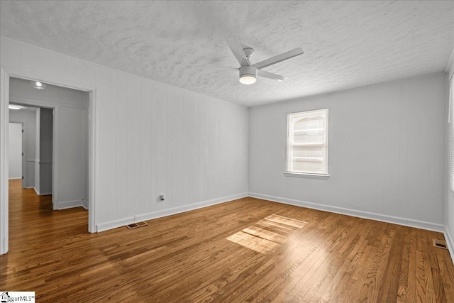 empty room featuring a textured ceiling, wood finished floors, visible vents, and a ceiling fan