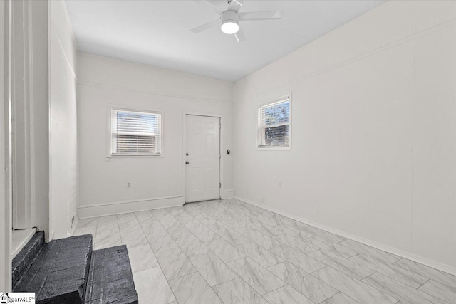 foyer featuring ceiling fan, marble finish floor, a wealth of natural light, and baseboards