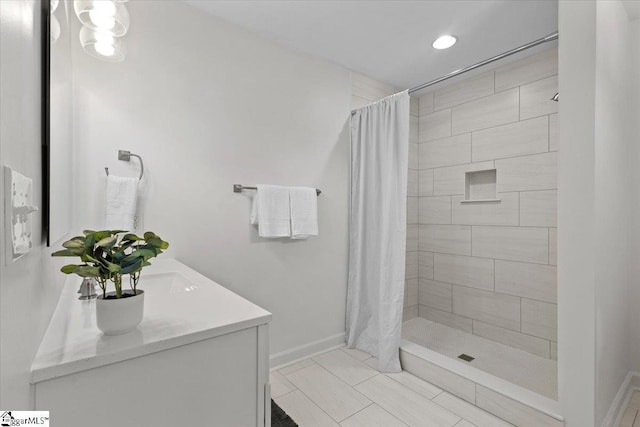 bathroom with double vanity, baseboards, and tiled shower