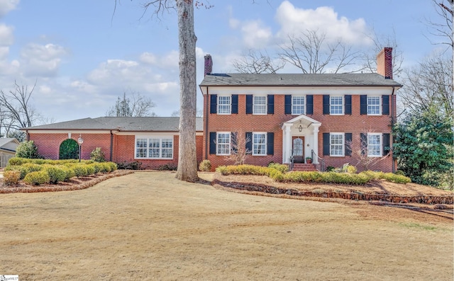 view of front facade with driveway, a chimney, and brick siding