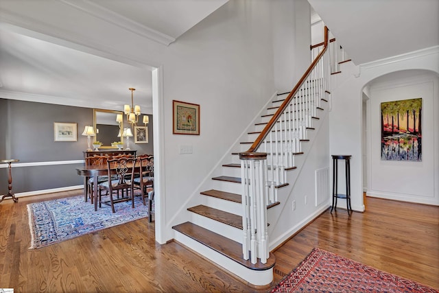 staircase featuring arched walkways, a notable chandelier, wood finished floors, and crown molding