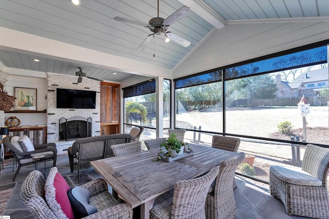 sunroom / solarium featuring vaulted ceiling with beams, ceiling fan, and an outdoor brick fireplace