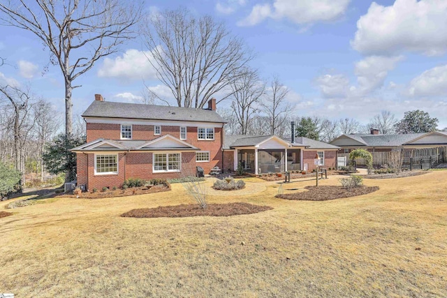 back of property with a sunroom, a chimney, a lawn, and brick siding