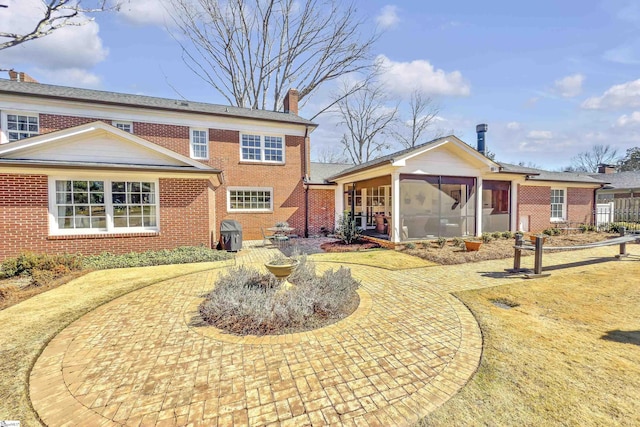 back of property with a sunroom, a chimney, and brick siding