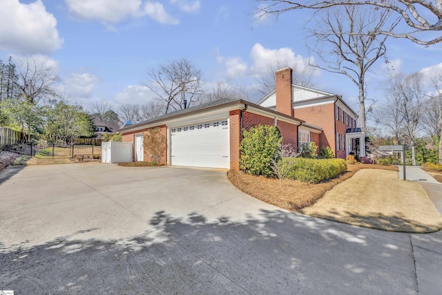 view of side of home with a garage, brick siding, fence, driveway, and a chimney