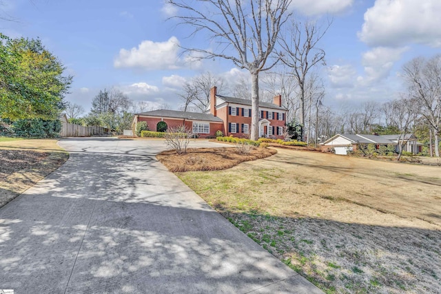 greek revival inspired property featuring a chimney, fence, a front lawn, and brick siding